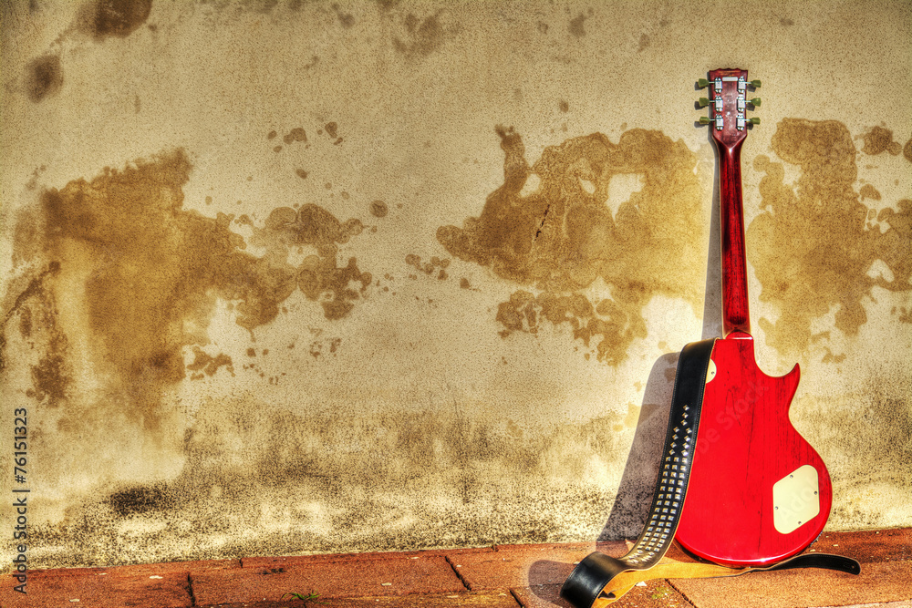 Obraz premium electric guitar leaned on a rustic wall in hdr