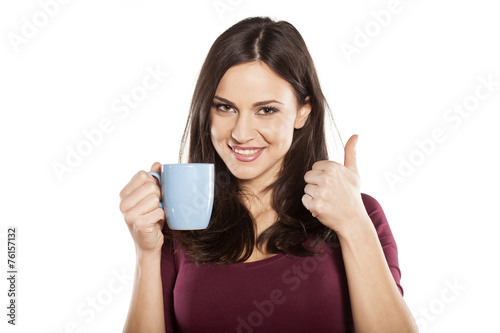 happy young woman holding a cup of  tea and showing thumbs up