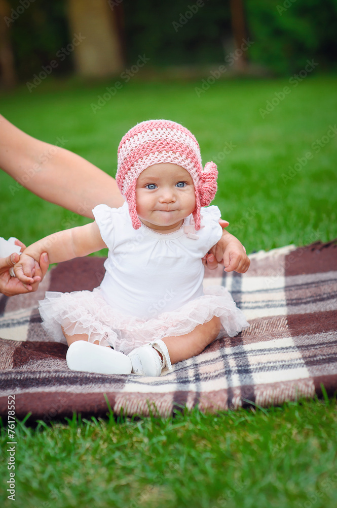 baby girl in pink knitted hat sitting on a rug in the park baby girl in pink knitted hat sitting on a rug in the park