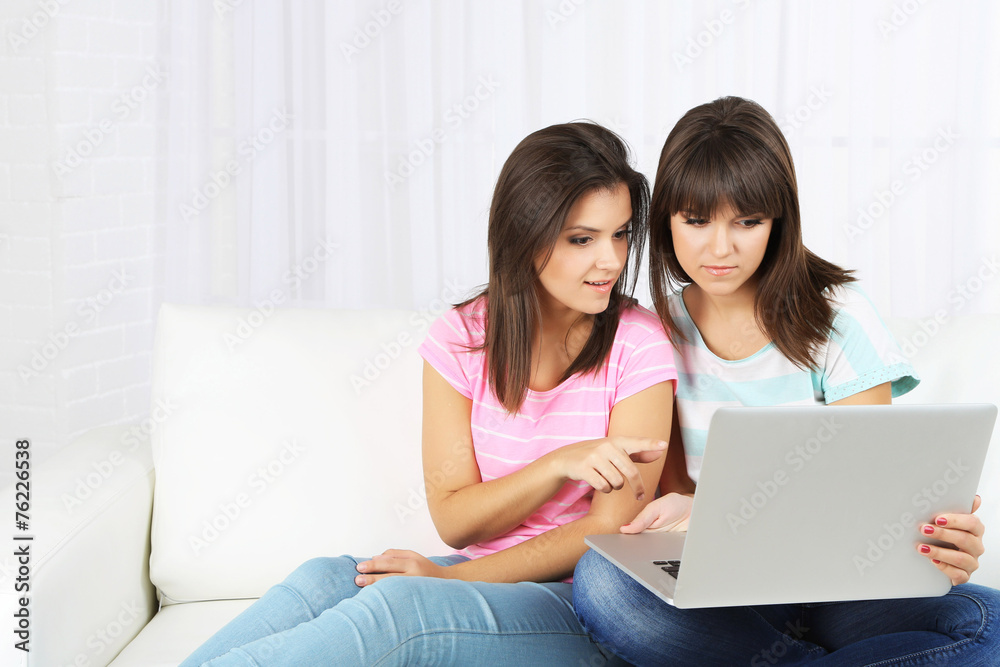 Beautiful girls twins sitting on sofa with notebook Beautiful girls twins sitting on sofa with notebook