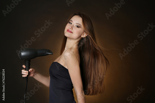 Beautiful young woman with long hair holding hair dryer