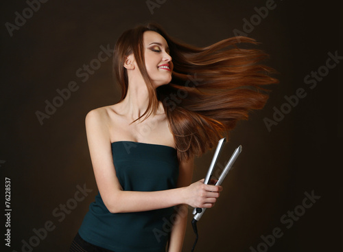 Beautiful young woman with long hair using hair straighteners