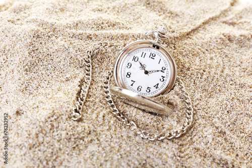 Silver pocket clock on sand background