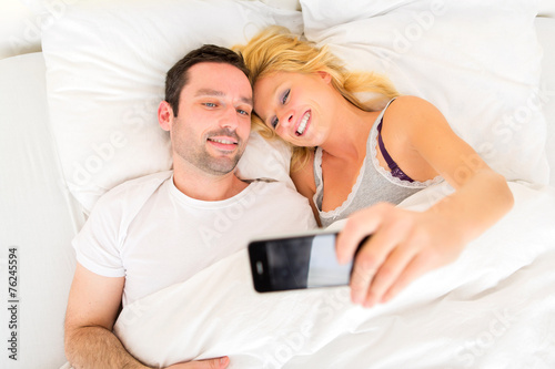 Young attracttive couple taking selfies in bed