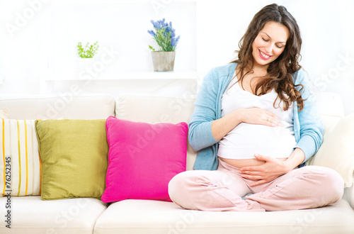 Pregnant woman sitting on a sofa and caressing her belly