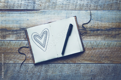 Old paper sketch book with hand-drown heart over vintage wooden