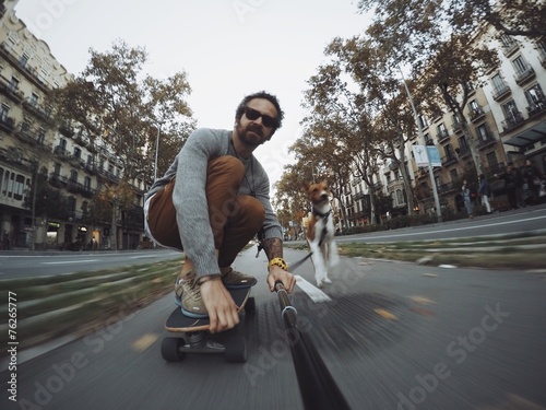 Man rides his skateboard followed by his dog photo