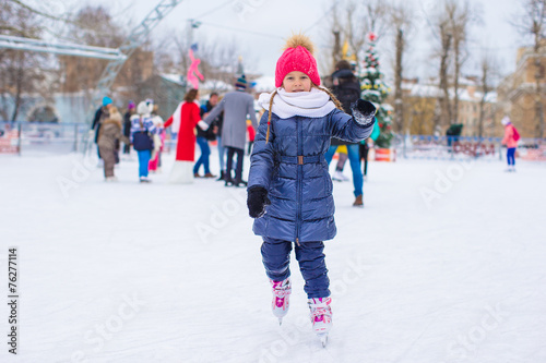 Cute little girl skating on the ice rink outdoors
