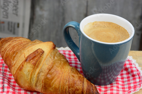 Coffee with croissant on old wooden table and newspaper