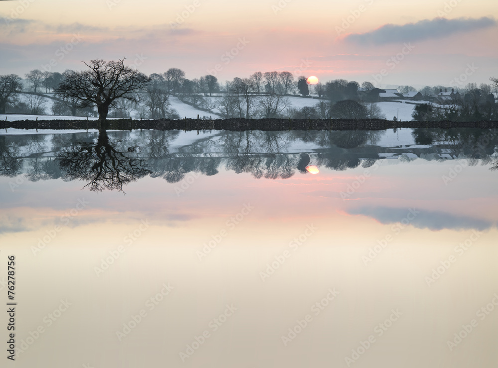 Snow covered Winter countryside sunrise landscape reflected in s