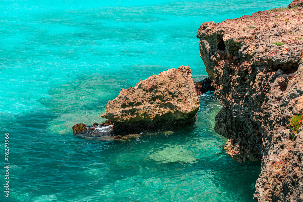 fragment of a cliff sitting in azure turquoise ocean water