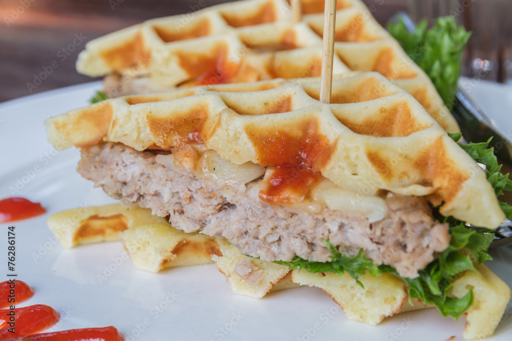 Hamburger made with waffles and pork on white plate.