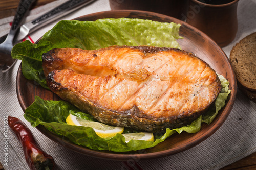 Baked trout steak in pottery with salad and slices of lemon