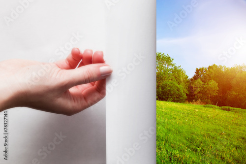 Foto Hand pulling edge of a paper to uncover, reveal green landscape