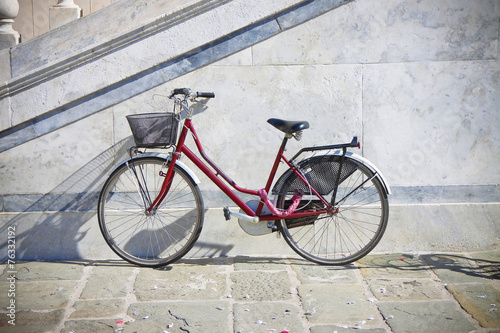 Red bicycle with basket against a marble wall