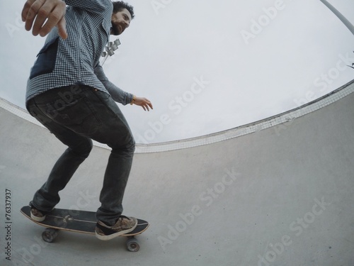 Fototapeta Athlete sporty man rides his skateboard in pool of skatepark while training his