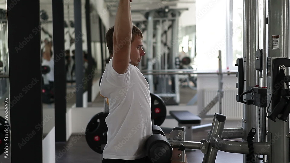 Fit man using the weights machine for his arms at the gym Fit man using the weights machine for his arms at the gym