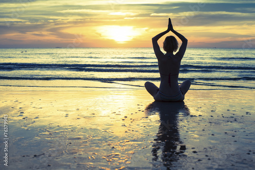 Woman practicing yoga on the beach at sunset in Thailand.