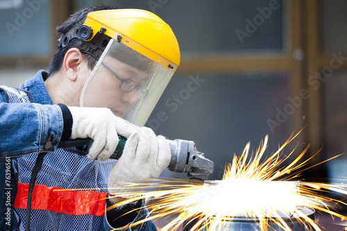 worker with grinder machine cutting metal in factory photo