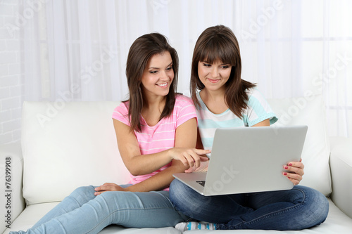 Beautiful girls twins sitting on sofa with notebook