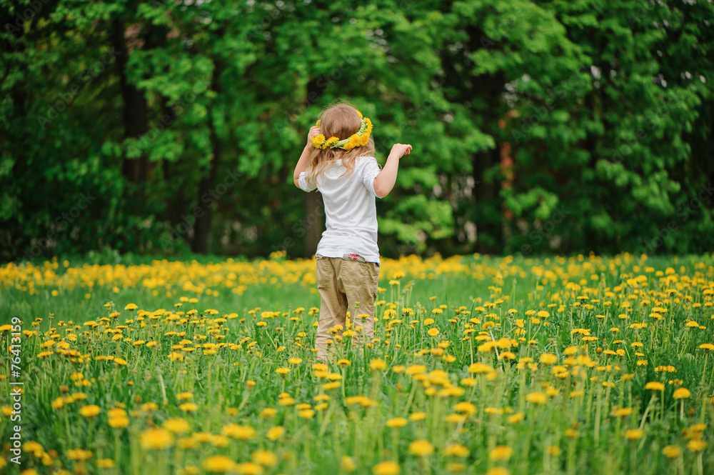 Fototapeta premium child girl in wreath walks on spring dandelion field