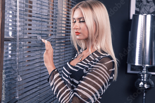 Adult woman with blonde hair stanging near window