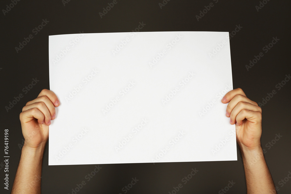 Blank sheet of paper in male hands on dark background Blank sheet of paper in male hands on dark background