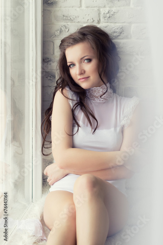 beautiful girl with long hair in white body sits  home by window