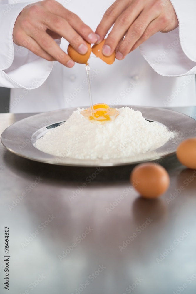 Close up of baker breaking eggs into flour Close up of baker breaking eggs into flour