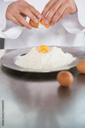 Close up of baker breaking eggs into flour