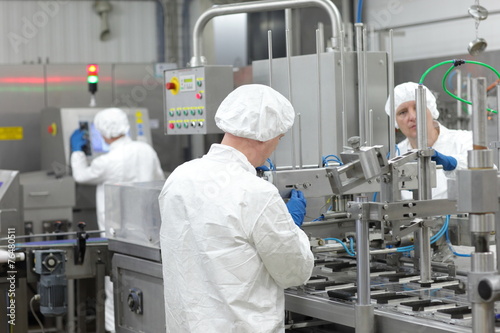 three workers in uniforms at production line in plant