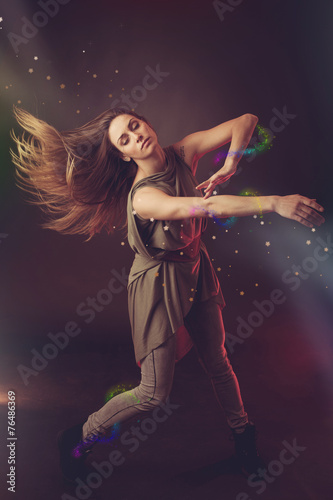 Beautiful woman dancer dancing over dark background with light r