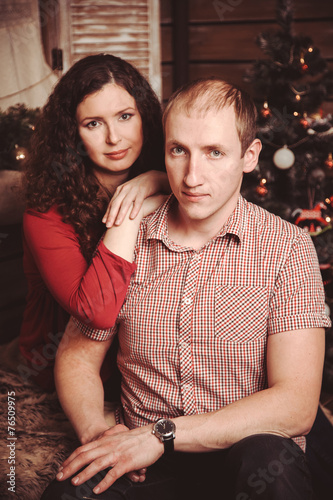 wife embraces her husband sitting in the New Year rustic interio