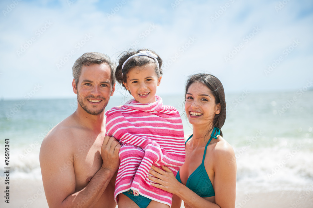 A couple at the beach posing in swimsuits with their daughter A couple at the beach posing in swimsuits with their daughter