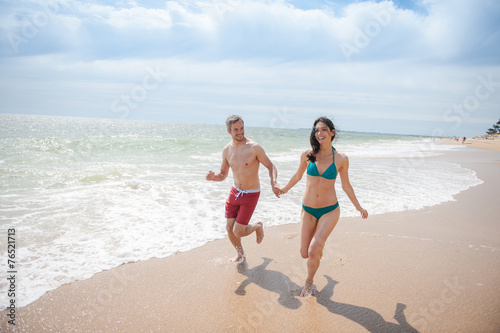 A young couple runs in the sea waves in swimsuit