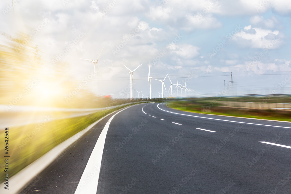 Fototapeta premium Wind turbines on landscape along empty road against sky