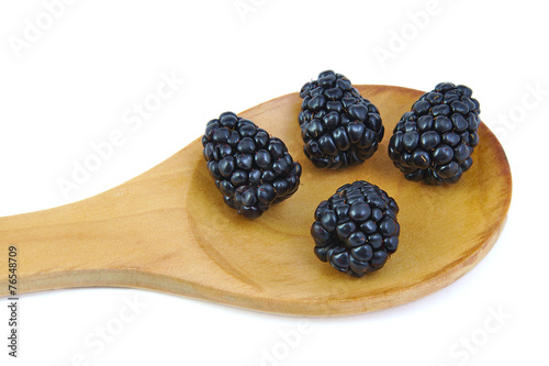 Four ripe blackberries in a wooden spoon.