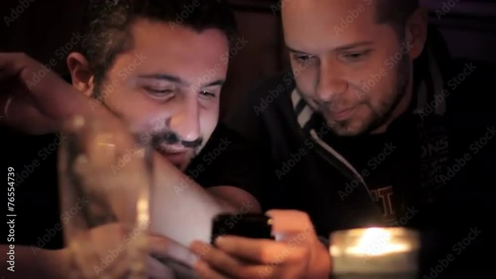 Two cherful men with Mobile Phone in a pub at night