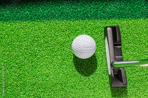 Golf club and golf ball on green grass background.