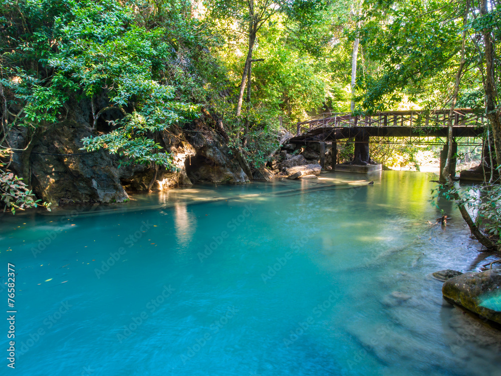 Naklejka premium River flowing through from Erawan waterfall in deep forest of national park, Thailand with a bridge background.