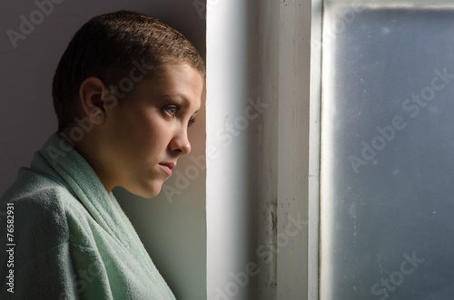 Young cancer patient standing in front of hospital window photo