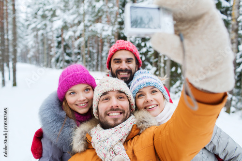 smiling friends with camera in winter forest