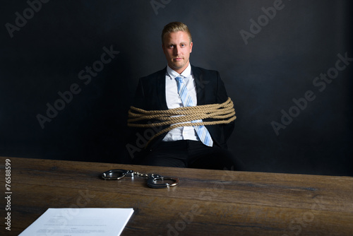 Businessman Tied With Rope Sitting In Front Of Table photo