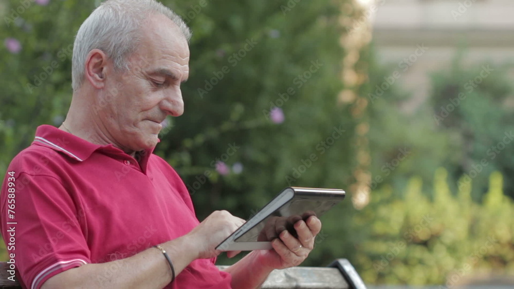 Old Man relaxing using tablet in park Old Man relaxing using tablet in park