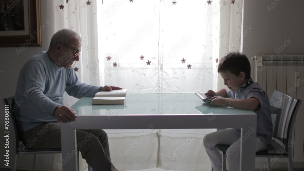 grandfather reads a book while baby reads a ebook with his tablet grandfather reads a book while baby reads a ebook with his tablet