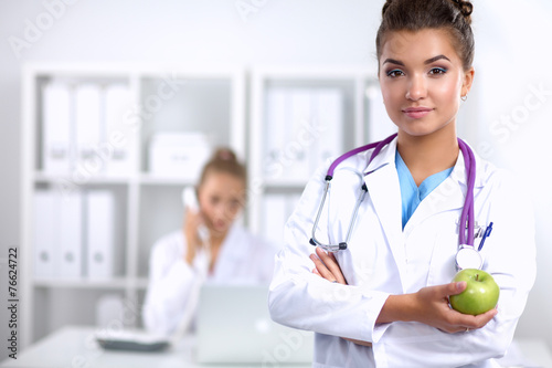 Smiling female doctor with green apple in uniform standing at