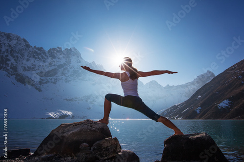 Young woman is practicing yoga at mountain lake