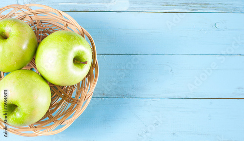 Green apples in basket on blue wood background