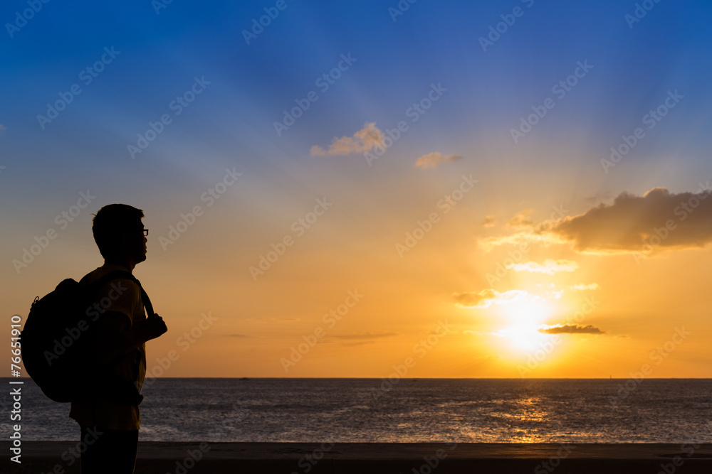 Silhouette traveler with backpack standing near the beach at sun