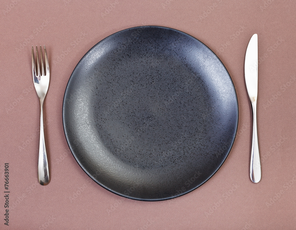 top view of black plate, fork, knife set on brown top view of black plate, fork, knife set on brown